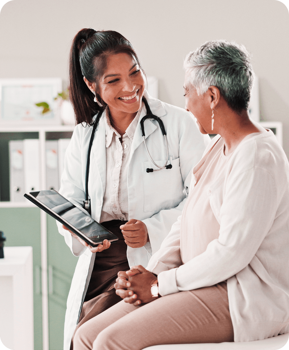 Female doctor smiling and holding a tablet while talking with a patient in a medical office.